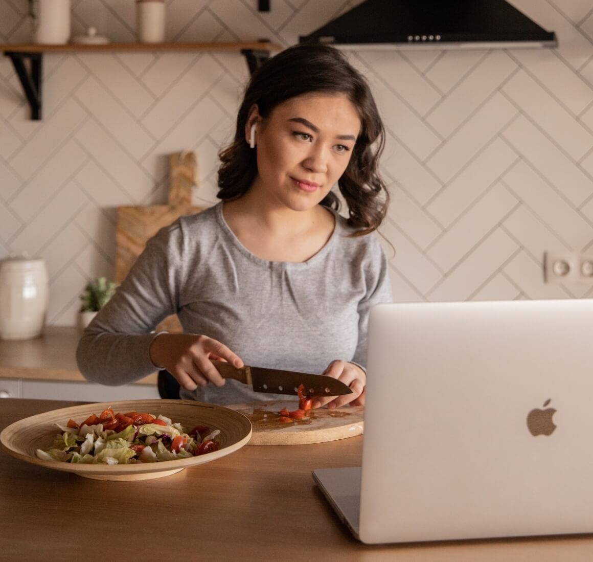 woman chopping vegetables and looking at laptop